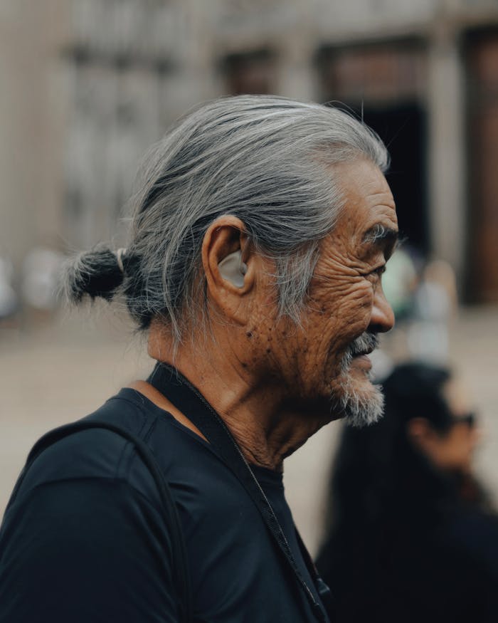Side profile of a senior man with a hearing aid enjoying a sunny day outdoors.