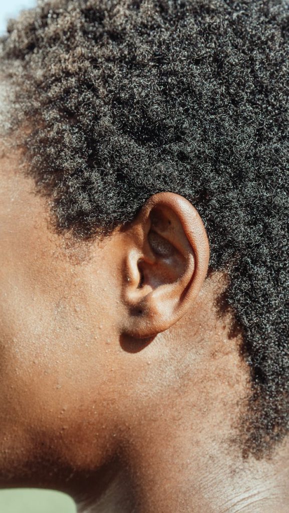 Detailed close-up of an ear showcasing natural textured hair in bright sunlight.